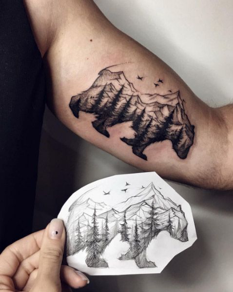 Tatuaje de un oso con un paisaje de montaña en el bíceps izquierdo