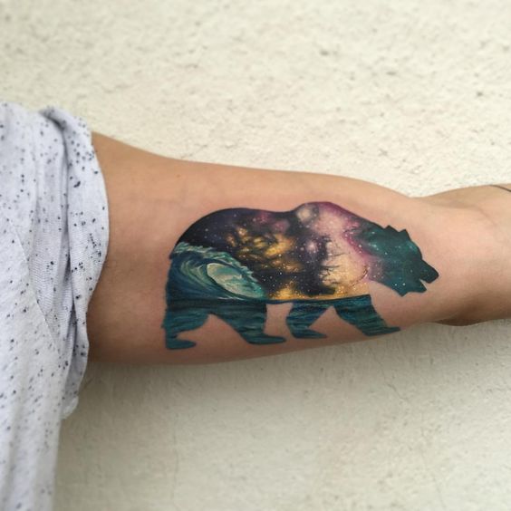 Oso con tatuaje de paisaje cósmico en el bíceps izquierdo